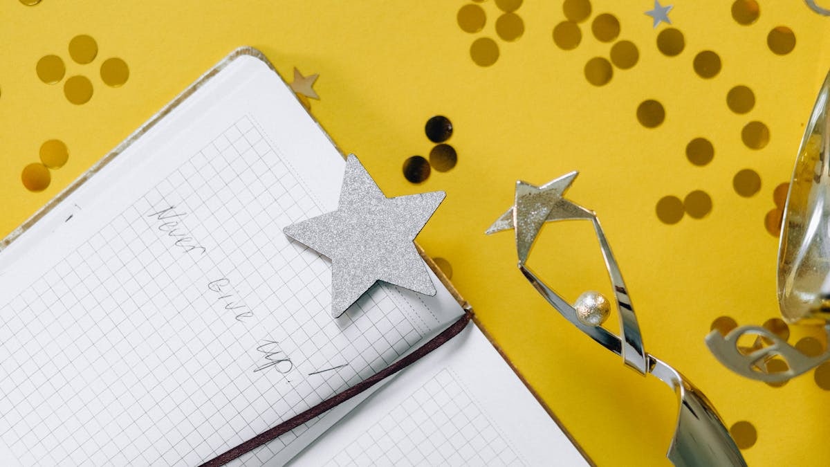 Flat lay of a notebook with motivational text, trophy, and star confetti on a yellow background.